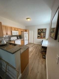 kitchen with kitchen peninsula, backsplash, white appliances, light hardwood / wood-style floors, and dark stone countertops