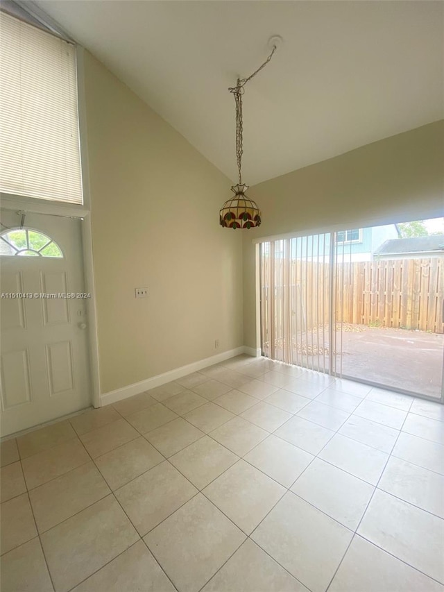 empty room with lofted ceiling, plenty of natural light, and light tile floors