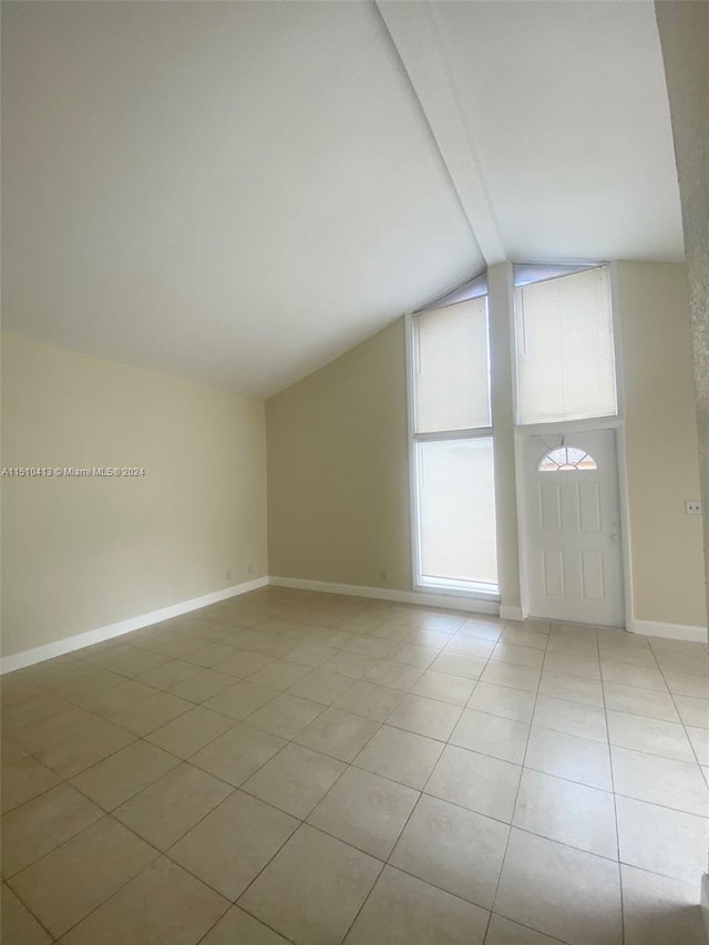 tiled spare room featuring lofted ceiling with beams
