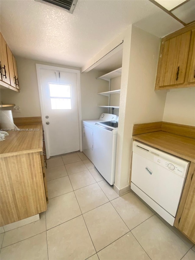 laundry room with a textured ceiling, washing machine and dryer, and light tile floors