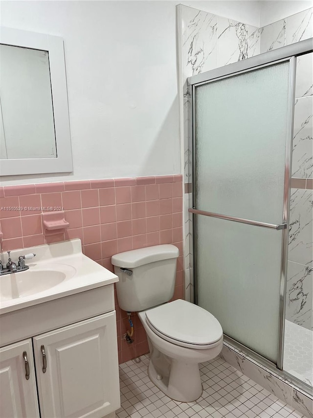 bathroom featuring a shower with door, vanity, toilet, and tile walls