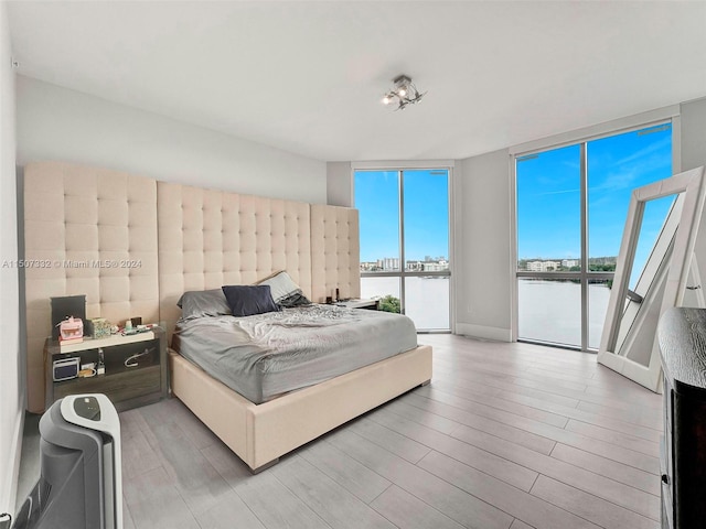 bedroom with expansive windows, a water view, light wood-type flooring, and access to exterior