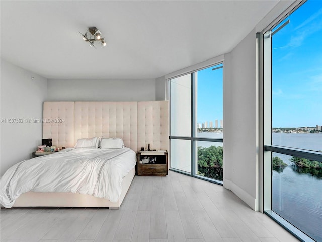 bedroom with light hardwood / wood-style floors, a wall of windows, and a water view