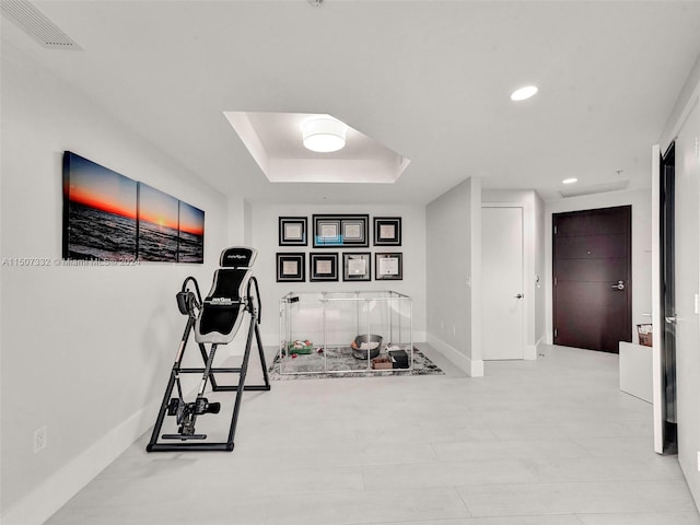 workout area featuring a raised ceiling and light tile floors