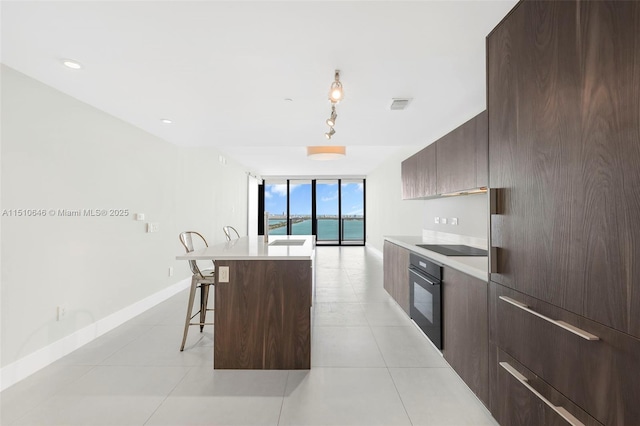 kitchen with light tile patterned floors, black appliances, a kitchen island, a breakfast bar area, and expansive windows