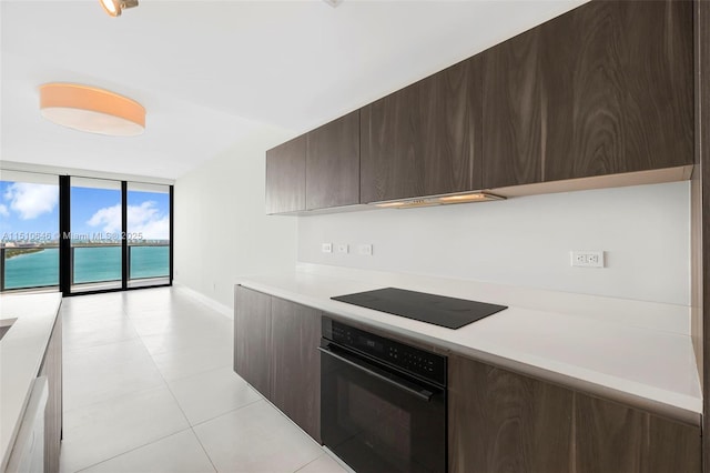 kitchen featuring a water view, light tile patterned floors, a wall of windows, dark brown cabinets, and black appliances