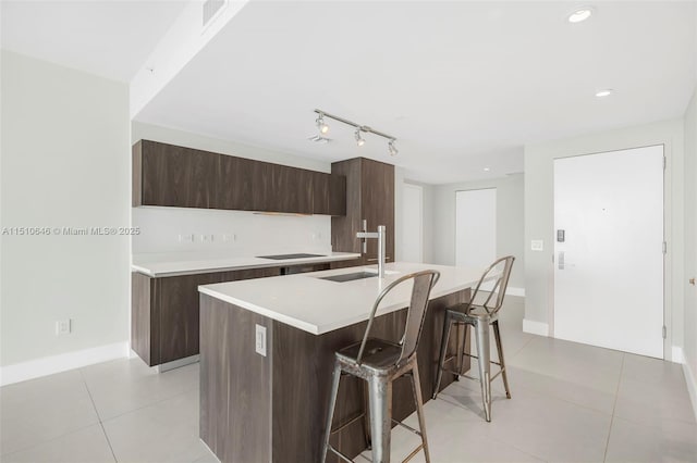 kitchen featuring sink, a kitchen island with sink, light tile patterned floors, black electric cooktop, and a breakfast bar