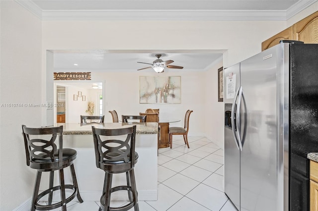 kitchen featuring a kitchen bar, stainless steel fridge, crown molding, light tile patterned flooring, and ceiling fan