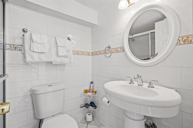 bathroom featuring a textured ceiling, toilet, and tile walls