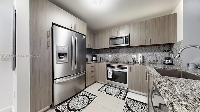 kitchen featuring sink, decorative backsplash, stainless steel appliances, and dark stone counters