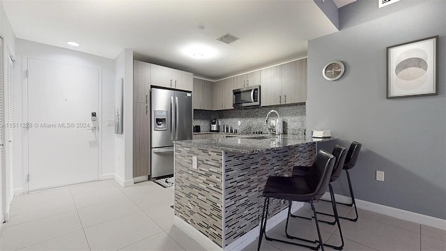 kitchen featuring tasteful backsplash, kitchen peninsula, stainless steel appliances, dark stone counters, and light tile patterned floors