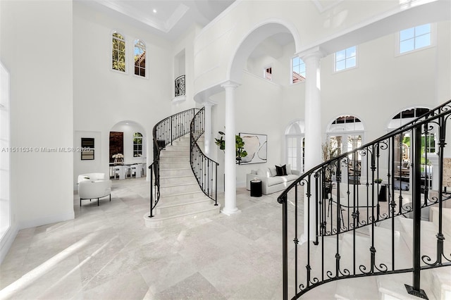 entrance foyer featuring plenty of natural light, a towering ceiling, ornamental molding, and ornate columns