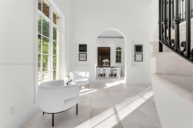 corridor with arched walkways, baseboards, a high ceiling, and stairway
