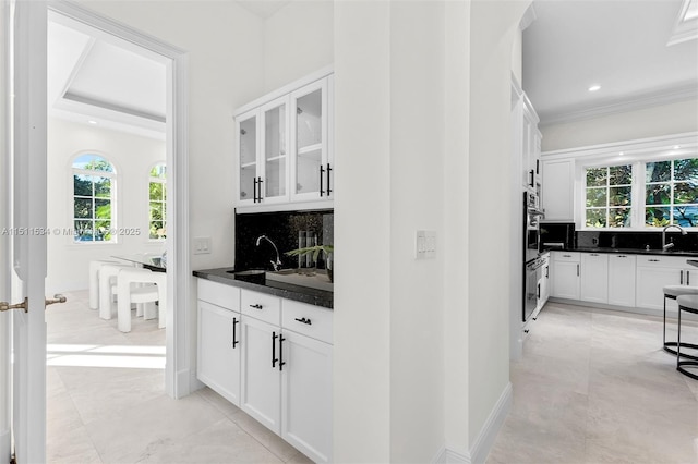 bar with decorative backsplash, white cabinetry, sink, and dark stone countertops