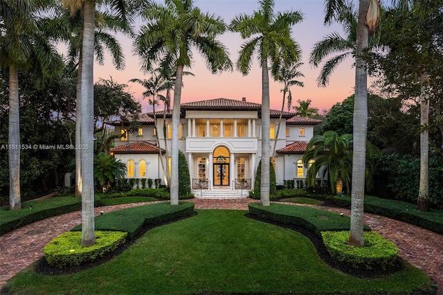 mediterranean / spanish home featuring french doors, a front yard, curved driveway, and stucco siding