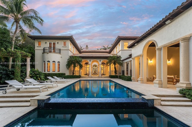 rear view of property with a balcony, a patio area, a pool with connected hot tub, french doors, and stucco siding