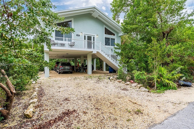 back of property featuring dirt driveway, stairway, a porch, a carport, and stucco siding