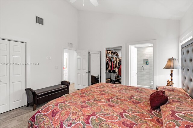 bedroom featuring light hardwood / wood-style floors, high vaulted ceiling, two closets, ceiling fan, and ensuite bathroom