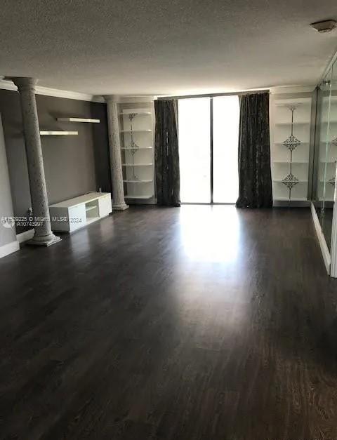 unfurnished living room featuring dark wood-type flooring, a textured ceiling, and ornate columns