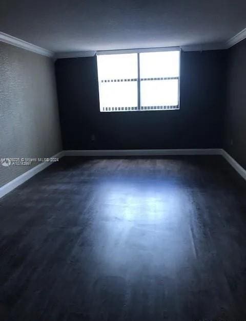 empty room with crown molding and dark wood-type flooring