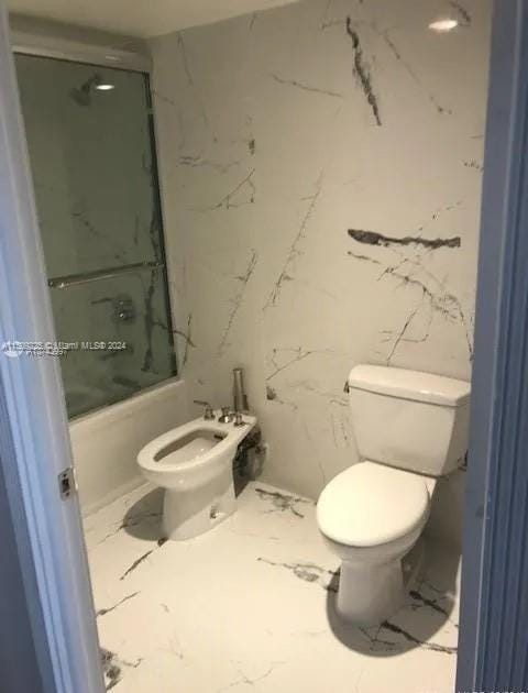 bathroom featuring a bidet, bath / shower combo with glass door, and toilet