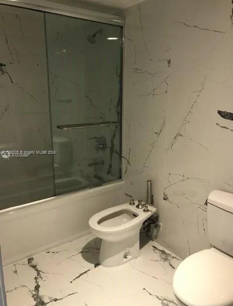 bathroom featuring a bidet, toilet, and shower / bath combination with glass door