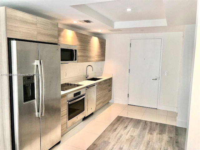 kitchen with a tray ceiling, stainless steel appliances, sink, and light tile floors