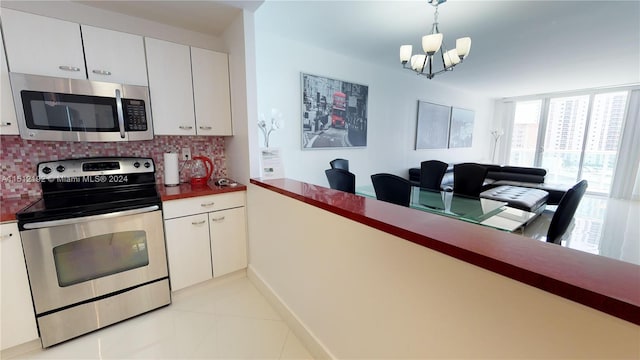 kitchen featuring light tile floors, backsplash, stainless steel appliances, an inviting chandelier, and white cabinetry