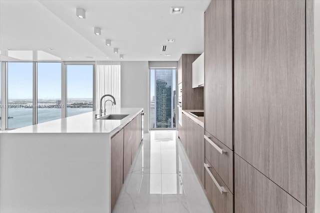 kitchen with a kitchen island with sink, sink, light tile floors, expansive windows, and a water view