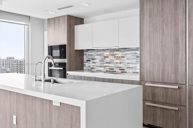 kitchen with white cabinetry, black appliances, a kitchen island with sink, sink, and tasteful backsplash