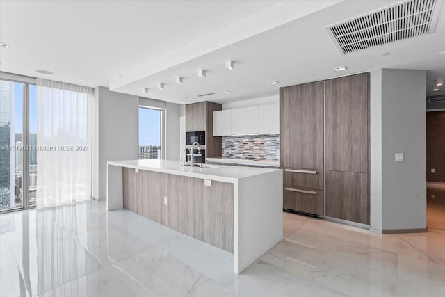 kitchen with white cabinetry, tasteful backsplash, light tile flooring, and a kitchen island with sink