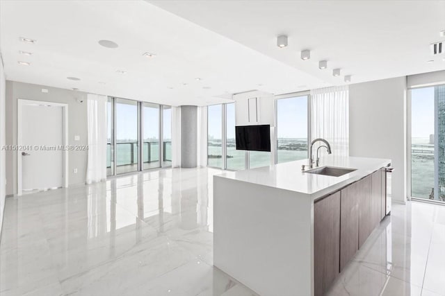 kitchen featuring light tile floors, floor to ceiling windows, sink, and a kitchen island with sink