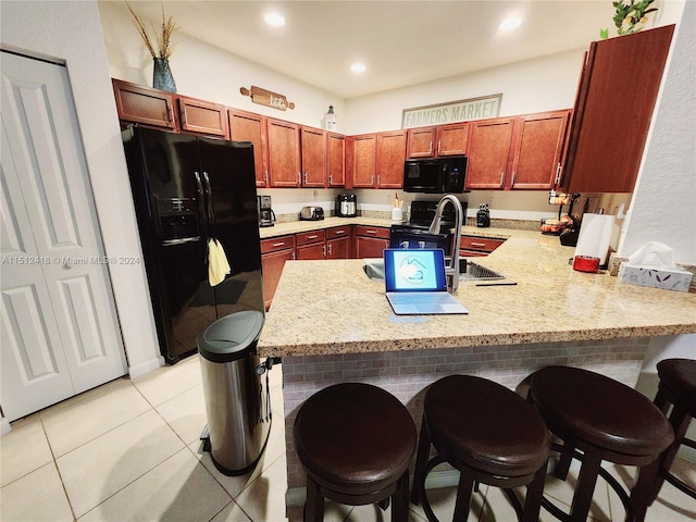 kitchen featuring kitchen peninsula, black appliances, light tile patterned floors, and a breakfast bar