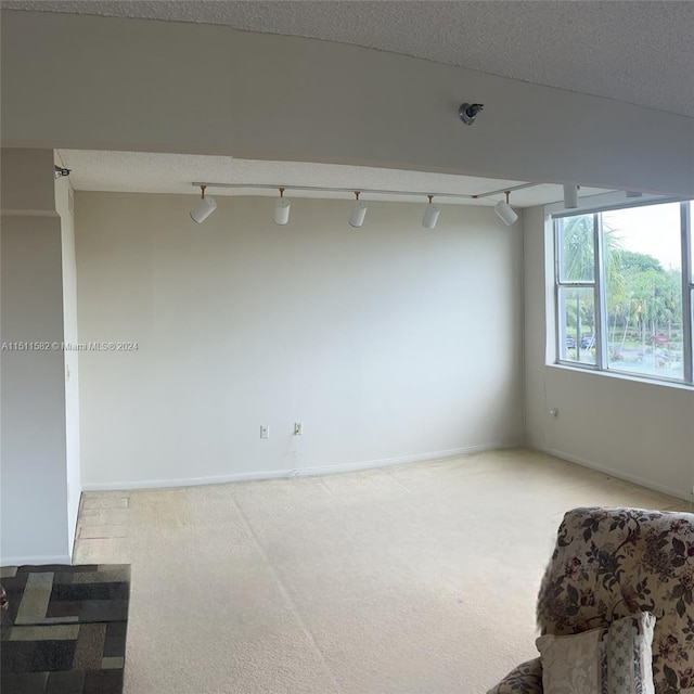 carpeted empty room with rail lighting and a textured ceiling