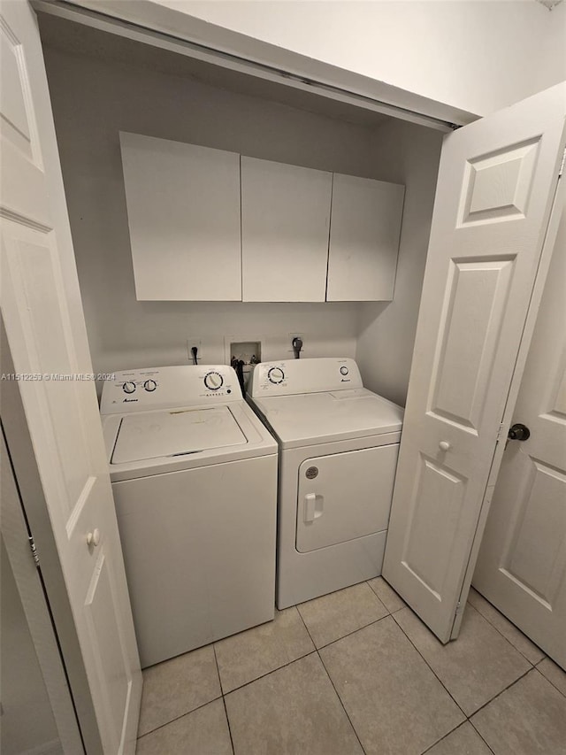 laundry room featuring washing machine and dryer, light tile patterned floors, and cabinets