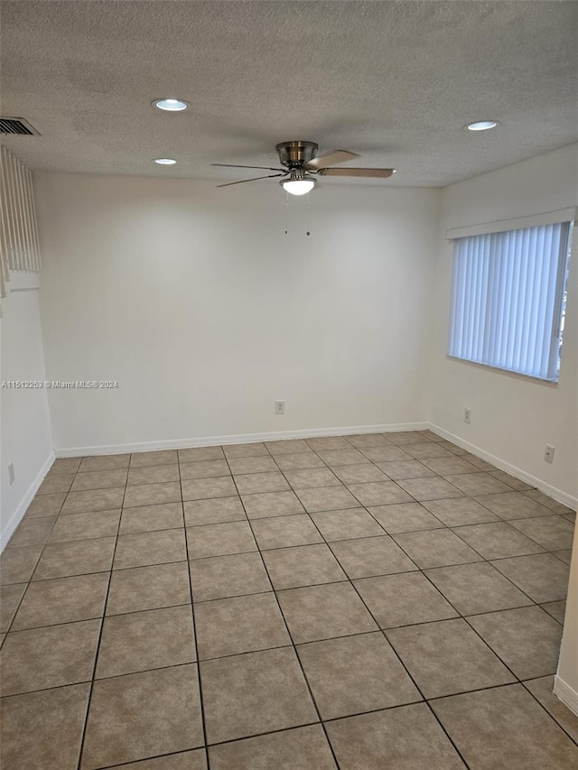 empty room with ceiling fan, light tile patterned floors, and a textured ceiling