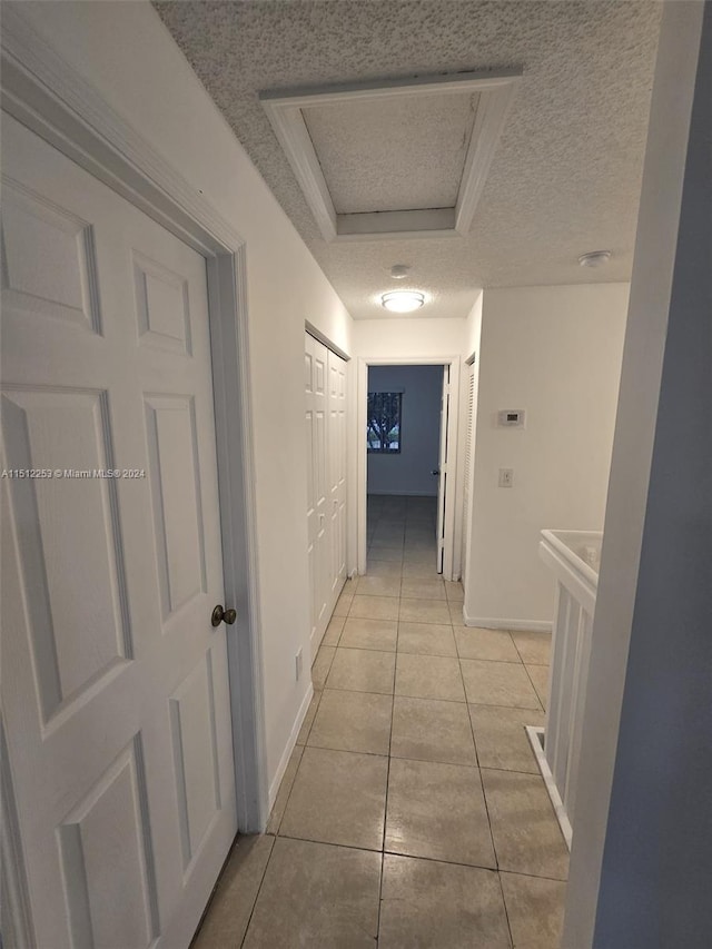 corridor featuring light tile patterned floors, a textured ceiling, and a tray ceiling