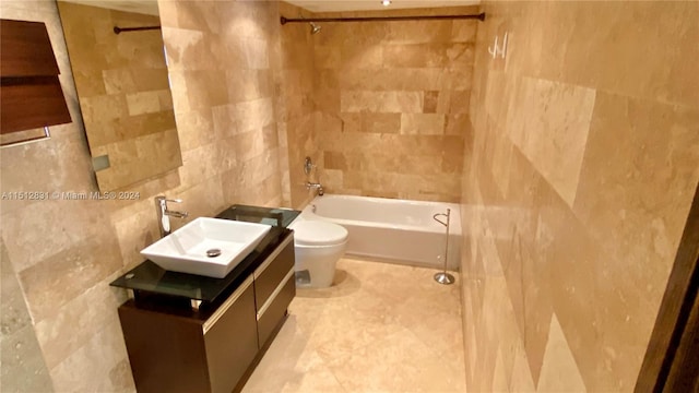 full bathroom featuring tiled shower / bath, vanity, toilet, and tile walls