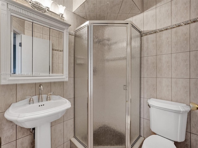 bathroom with tile walls, toilet, sink, and a shower with door