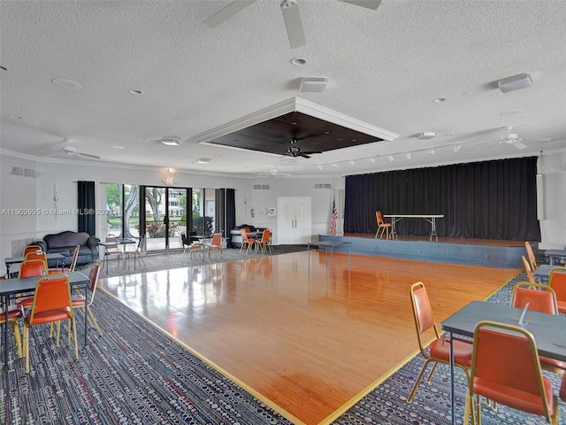 interior space with a textured ceiling, a raised ceiling, ornamental molding, hardwood / wood-style flooring, and ceiling fan