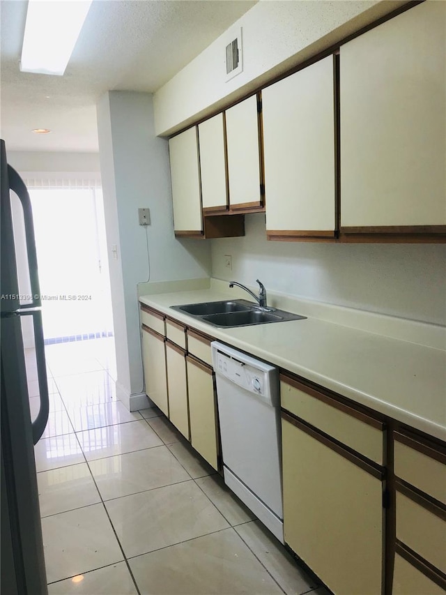 kitchen featuring white dishwasher, light tile floors, black refrigerator, white cabinetry, and sink