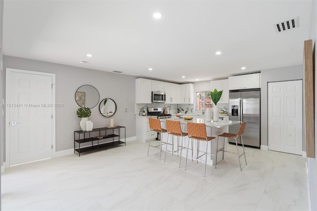 kitchen with a kitchen island, stainless steel appliances, a breakfast bar, white cabinets, and tasteful backsplash