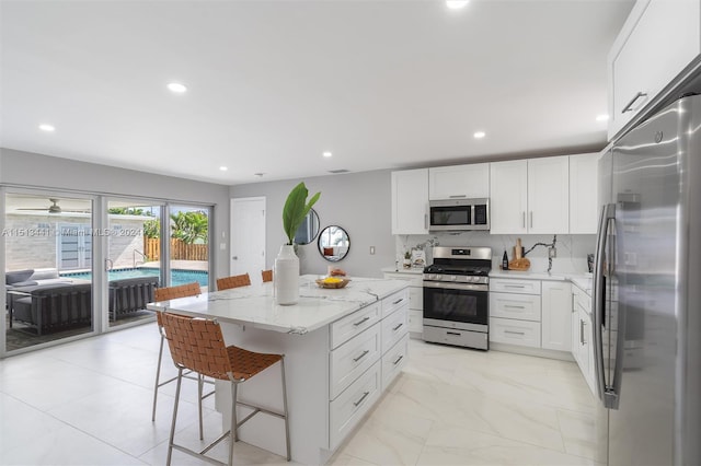 kitchen featuring white cabinets, a kitchen island, appliances with stainless steel finishes, light stone countertops, and a kitchen bar