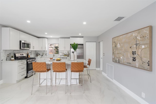 kitchen featuring appliances with stainless steel finishes, a kitchen bar, a kitchen island, backsplash, and white cabinets