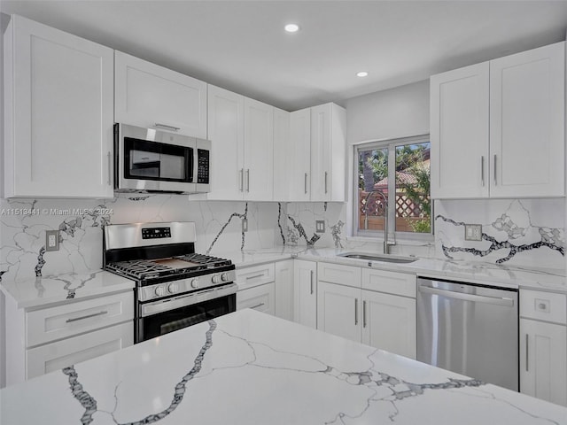 kitchen with appliances with stainless steel finishes, white cabinetry, light stone countertops, and sink