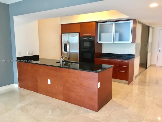 kitchen with stainless steel fridge, double oven, light tile flooring, sink, and dark stone counters