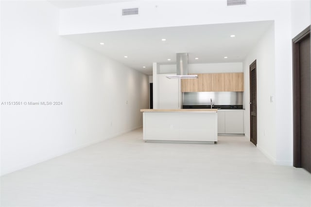 kitchen featuring an island with sink, white cabinets, island range hood, and light brown cabinets