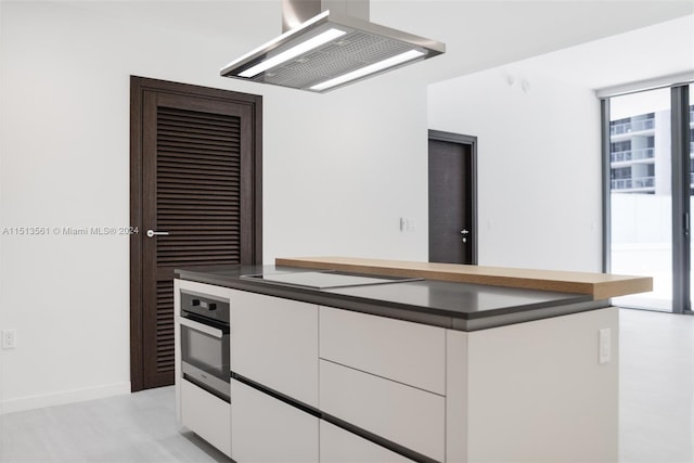 kitchen with black electric stovetop, oven, white cabinetry, and range hood