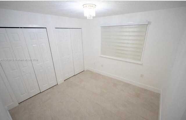 unfurnished bedroom featuring light carpet and multiple closets