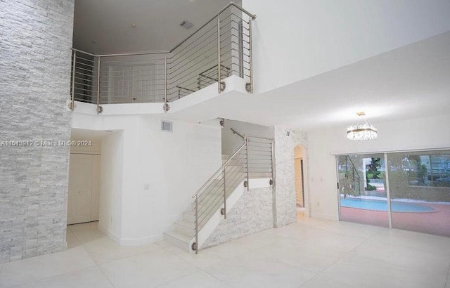 staircase featuring light tile floors, a high ceiling, and an inviting chandelier